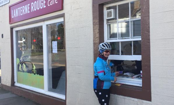 A female cyclists collects a takeaway coffee from a serving hatch at a roadside cafe