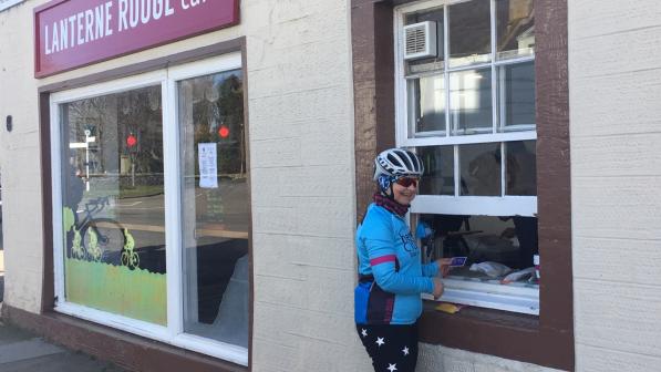 A female cyclists collects a takeaway coffee from a serving hatch at a roadside cafe