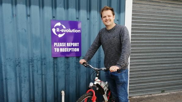 Man sands with his bicycle in front of a blue corrugated wall and a garage door