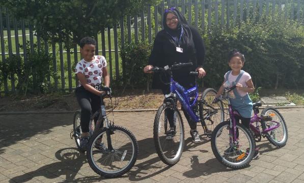 A woman and a boy and a girl pose with bicycles outside on a sunny day 
