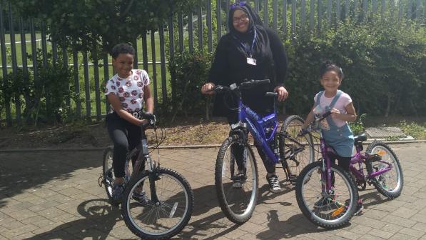 A woman and a boy and a girl pose with bicycles outside on a sunny day 
