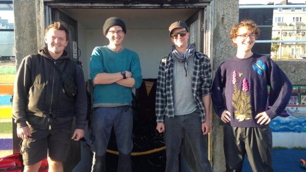 Four men stand in front of a shelter with a sign above it which says Labyrinth