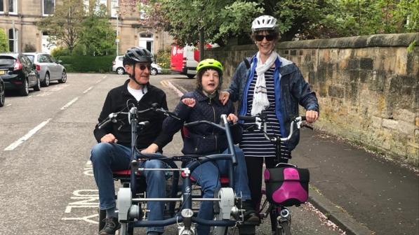 Father and daughter on side-by-side tandem with mother standing next to them on solo bike