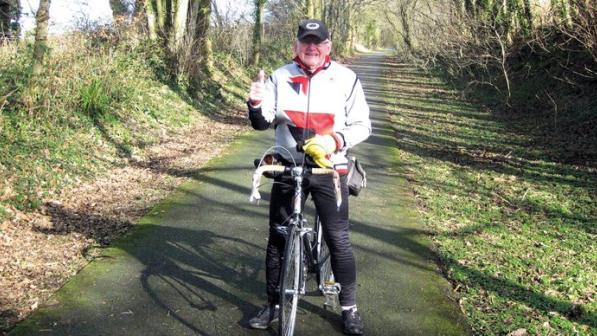 Man in white jacket with red stride gives a thumbs up while astride a bicycle 