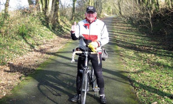 Man in white jacket with red stride gives a thumbs up while astride a bicycle 