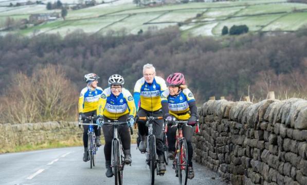 Four cyclists riding in two pairs up a hill with a stone wall to their left