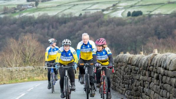 Four cyclists riding in two pairs up a hill with a stone wall to their left