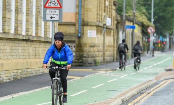 A woman in a blue jacket riding along a designated cycle lane with buildings to her right