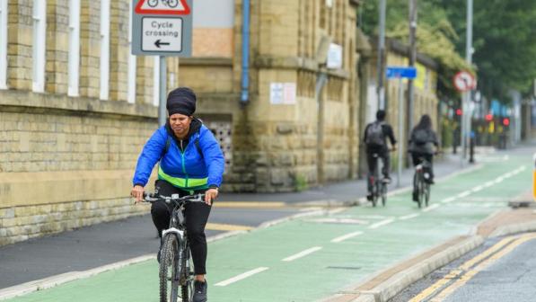 A woman in a blue jacket riding along a designated cycle lane with buildings to her right