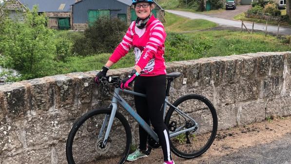 Woman with bike standing next to wall in rural setting