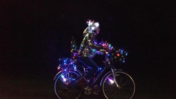 A woman riding a bike covered in Christmas lights.