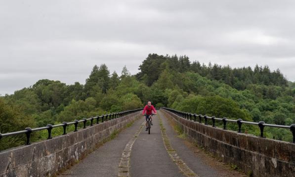 An image showing a distant woman in pink on a bicycle riding across a bridge toward the camera 