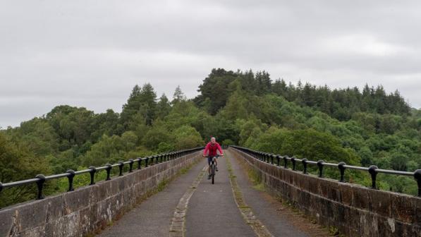 An image showing a distant woman in pink on a bicycle riding across a bridge toward the camera 