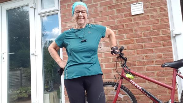 A woman wearing a azure fabric cycling top stands next to her bicycle on her patio