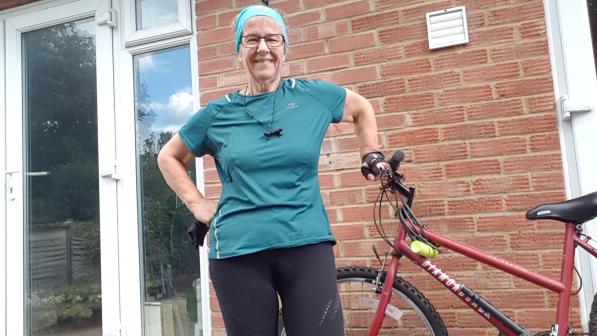 A woman wearing a azure fabric cycling top stands next to her bicycle on her patio 