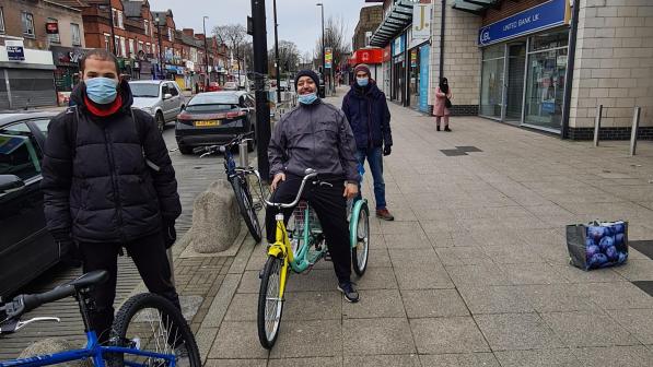 Three men spaces out and lined up along with pavement with bicycles standing close to a bus stop on a busy road