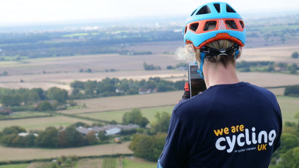 Female cyclist wearing Cycling UK t-shirt taking photo of stunning landscape on phone