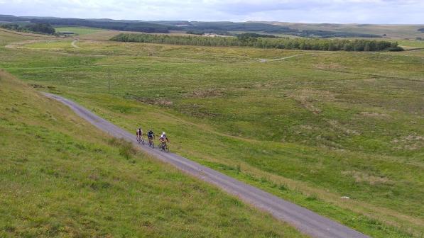 Three cyclists on a lane among rolling green hills