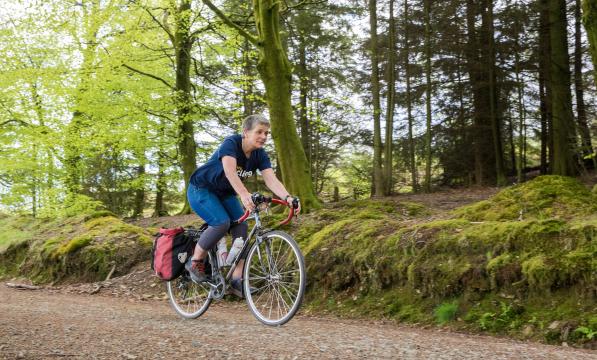 Woman smiling as she cycles down a gravel track through trees