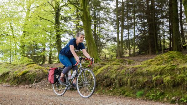 Woman smiling as she cycles down a gravel track through trees