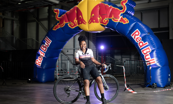 Woman leaning on a road bike while standing in front of a Red Bull branded arch