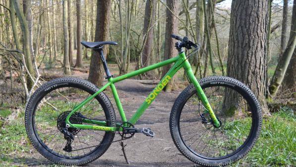 A rigid mountain bike stands in the middle of a woodland trail