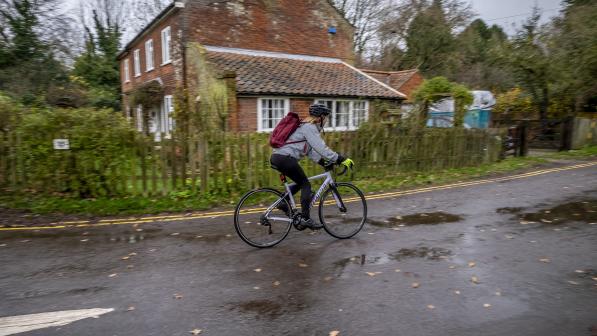 A woman cycles on a wet road with puddles and leaves scattered on it