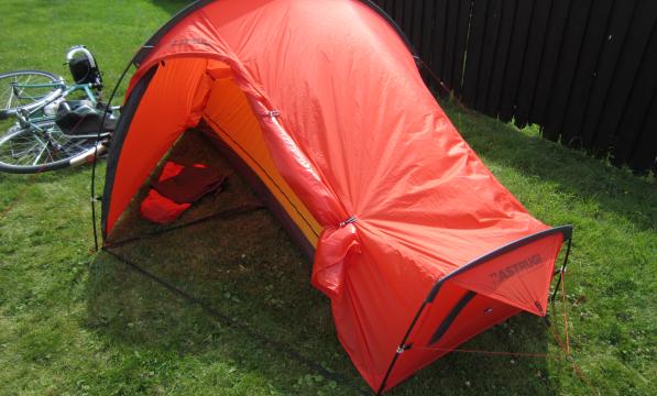 A bright orange 1-person tent is pitched up on grass