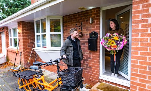 man with cargo bike making delivery of flowers to woman at door of house