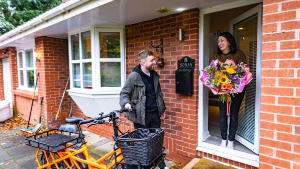 man with cargo bike making delivery of flowers to woman at door of house