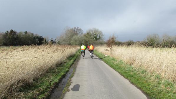 Two people cycling through a flat landscape