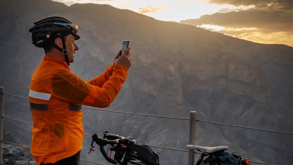 A man in cycling kit is standing next to his bike taking a photo