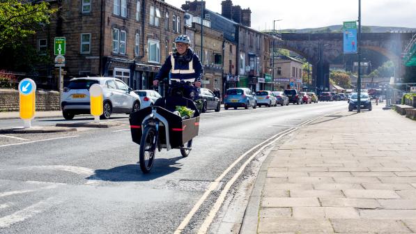 Person rides an e-cargo bike on the road, buildings in the background