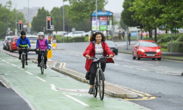 Three people pedal on green cycle lane next to busy road in the city