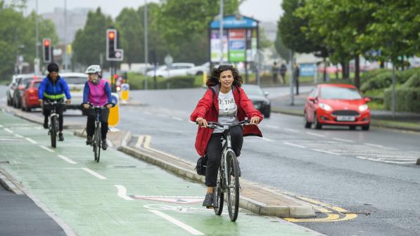 Three people pedal on green cycle lane next to busy road in the city