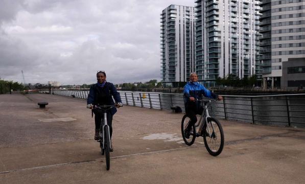 Two people pedalling next to MediaCity in Salford, Manchester prior to the Cycling made e-asy launch