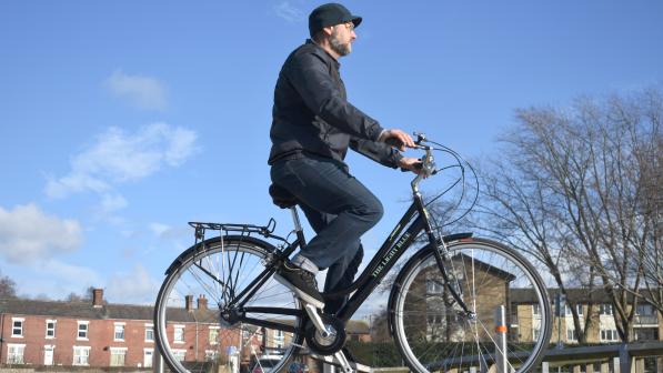 A man is riding a black step-through roadster along a suburban street