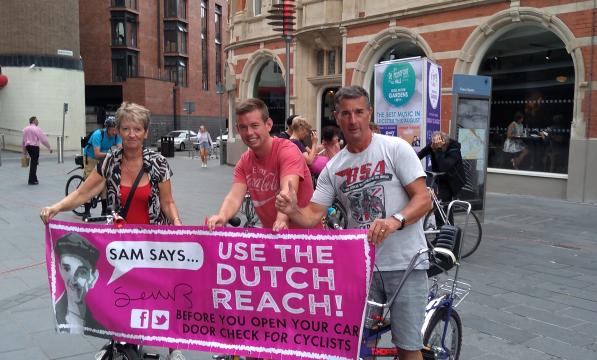 3 people hold banner, promoting the Dutch Reach to improve cycle safety