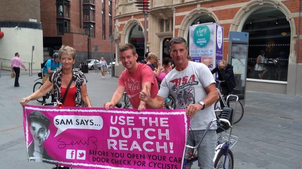 3 people hold banner, promoting the Dutch Reach to improve cycle safety