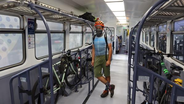 A man stands wearing a helmet. He‘s leaning against the pole in a train bicycle carriage in front of his gravel bike