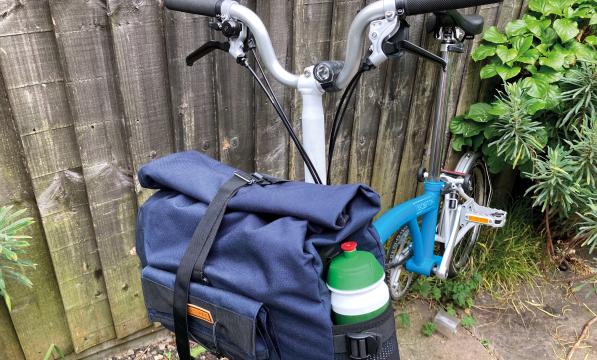 A utility bag hangs at the front of a Brompton bike, the foldable commuter-style bicycle