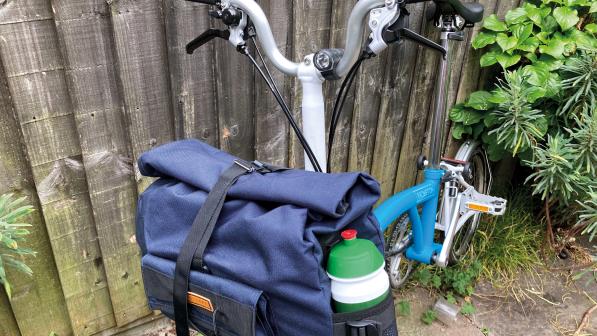 A utility bag hangs at the front of a Brompton bike, the foldable commuter-style bicycle