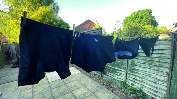 Four pairs of black padded cycling pants hang on a washing line in a garden