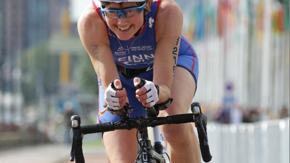 Kath competing in a road bike event. She is wearing a white helmet and blue lycra kit.