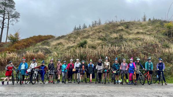 A group of women about to ride their bikes in the forest wearing party dresses.