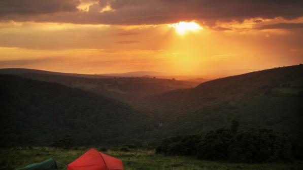 Small red tent pitched on a hill at sunset