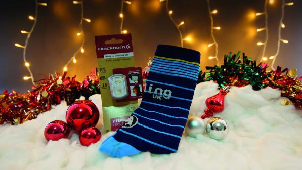 A pair of blue stripy socks display the Cycling UK logo. They lay next to a front bicycle light and are surrounded by christmas baubles and fairy lights