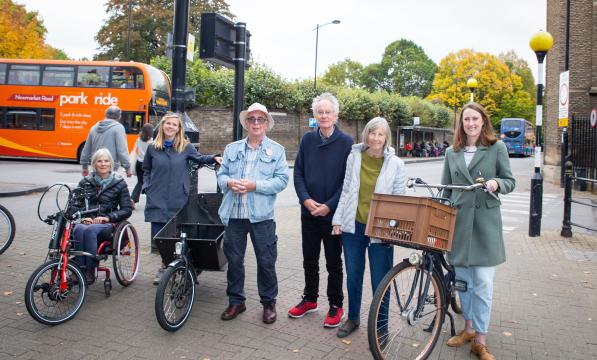 A mixture of men and woman stand with Roxanne. One woman is sat in a recumbent, one is stood next to a cargo bike, and Roxanne stands with a Dutch-style bicycle sporting a basket on the front