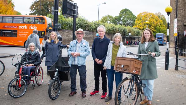 A mixture of men and woman stand with Roxanne. One woman is sat in a recumbent, one is stood next to a cargo bike, and Roxanne stands with a Dutch-style bicycle sporting a basket on the front