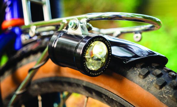 A dynamo light sits on the side of the mudguard of a bicycle wheel